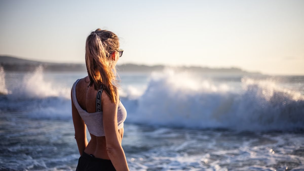 Back view of a woman enjoying the ocean waves on a beach during sunset.